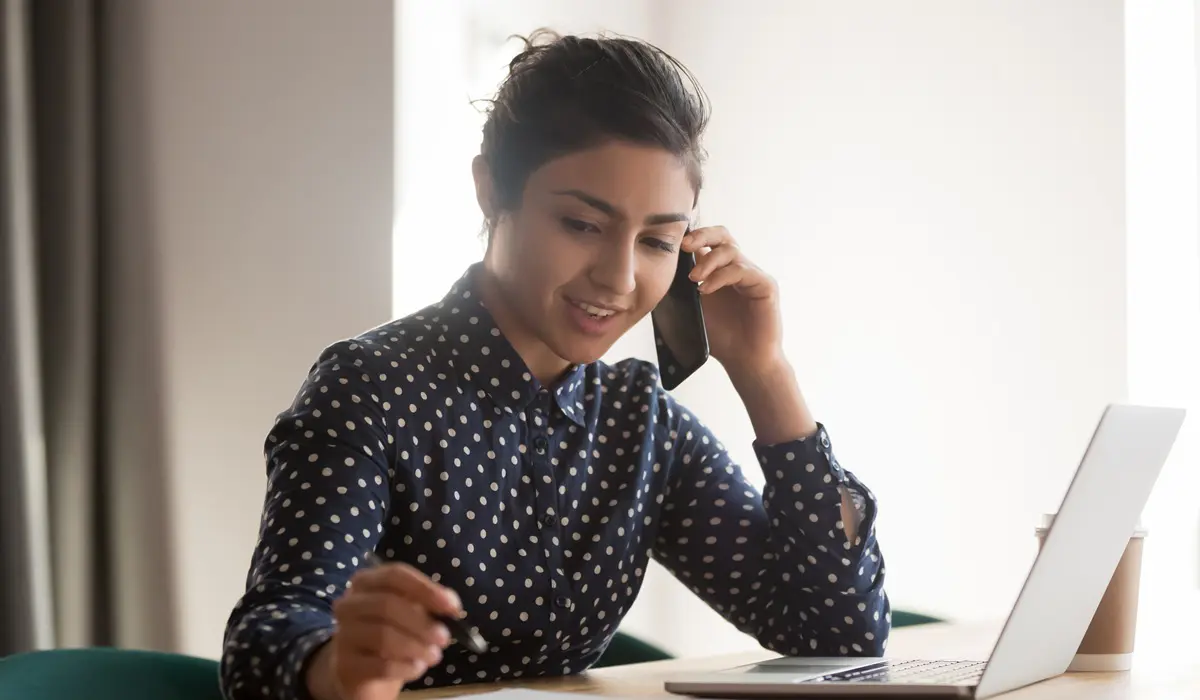 Busy female indian employee talk on cellphone at workplace