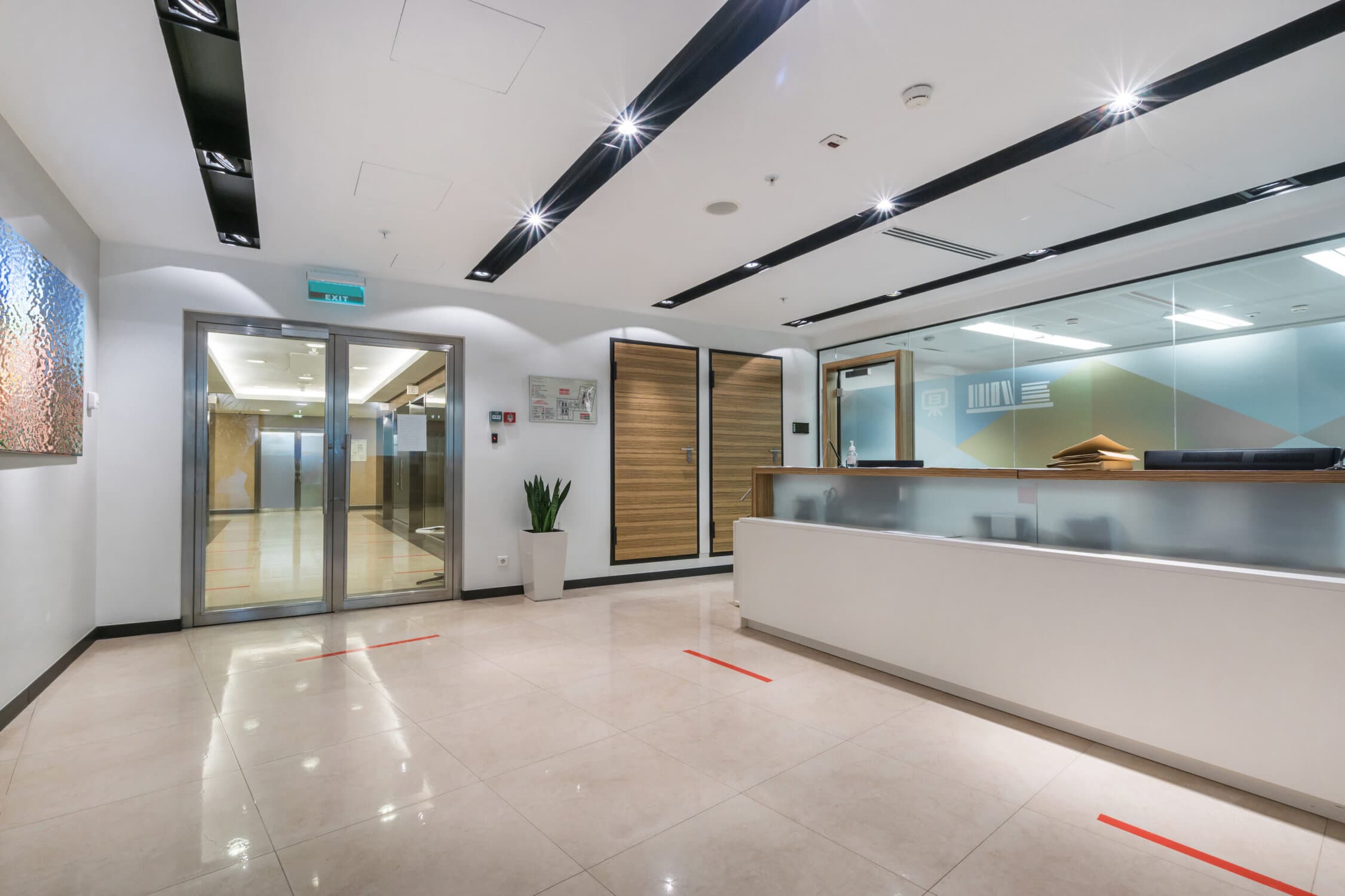 A spacious, bright office hall with a reception desk, glass doors and a picture on the wall.